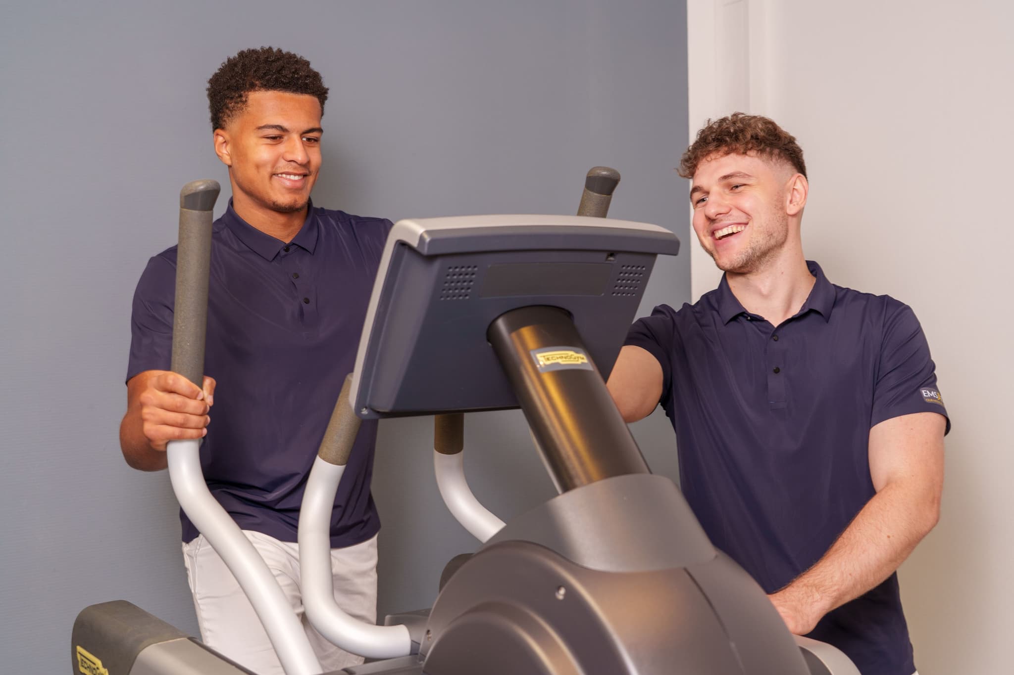 Zwei Trainer von EMS ONE am Crosstrainer im Studio, einer stellt das Trainingsprogramm am Display ein