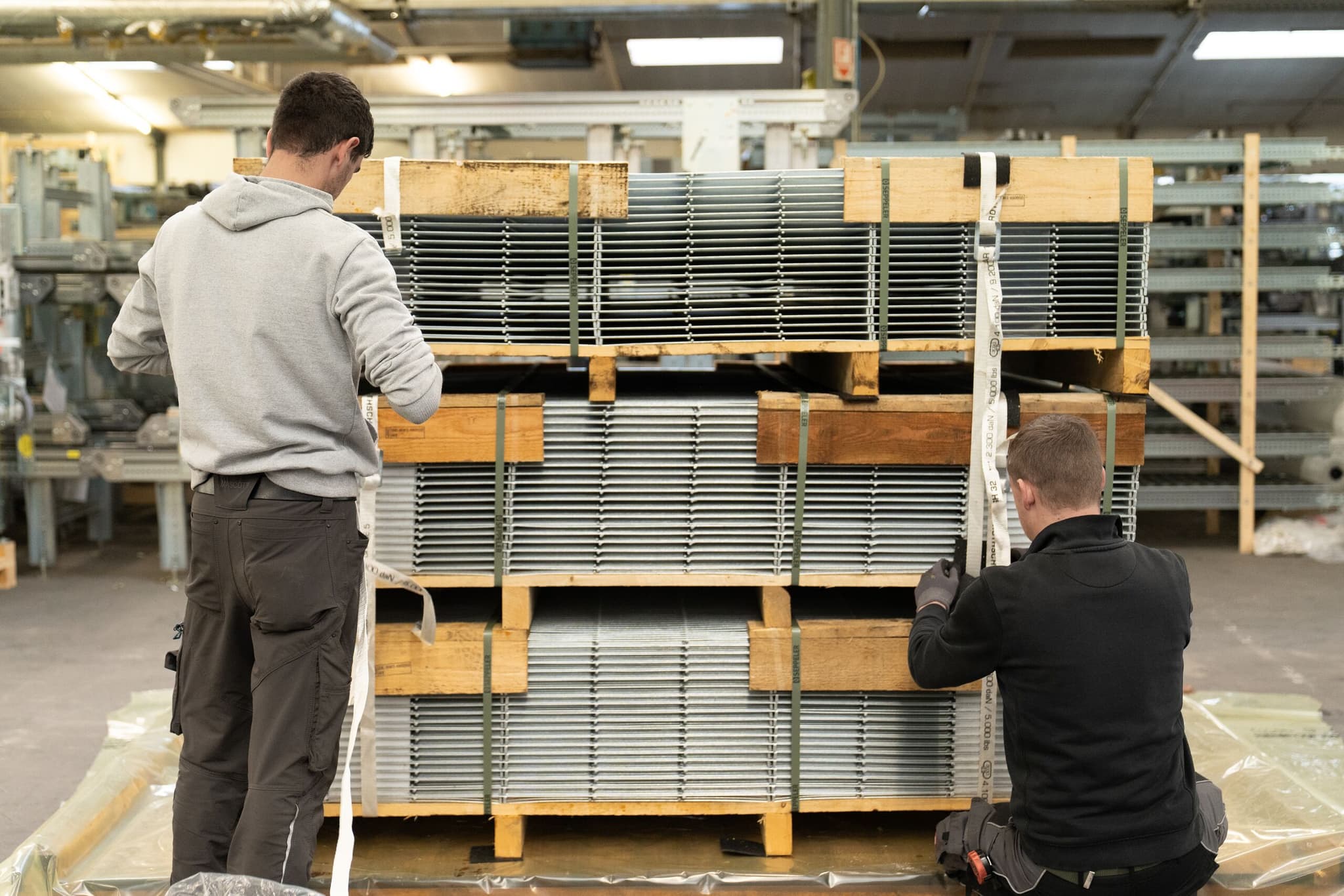 Zwei Mitarbeitende der MHS GmbH sichern gestapelte Gitterroste mit Spanngurten
