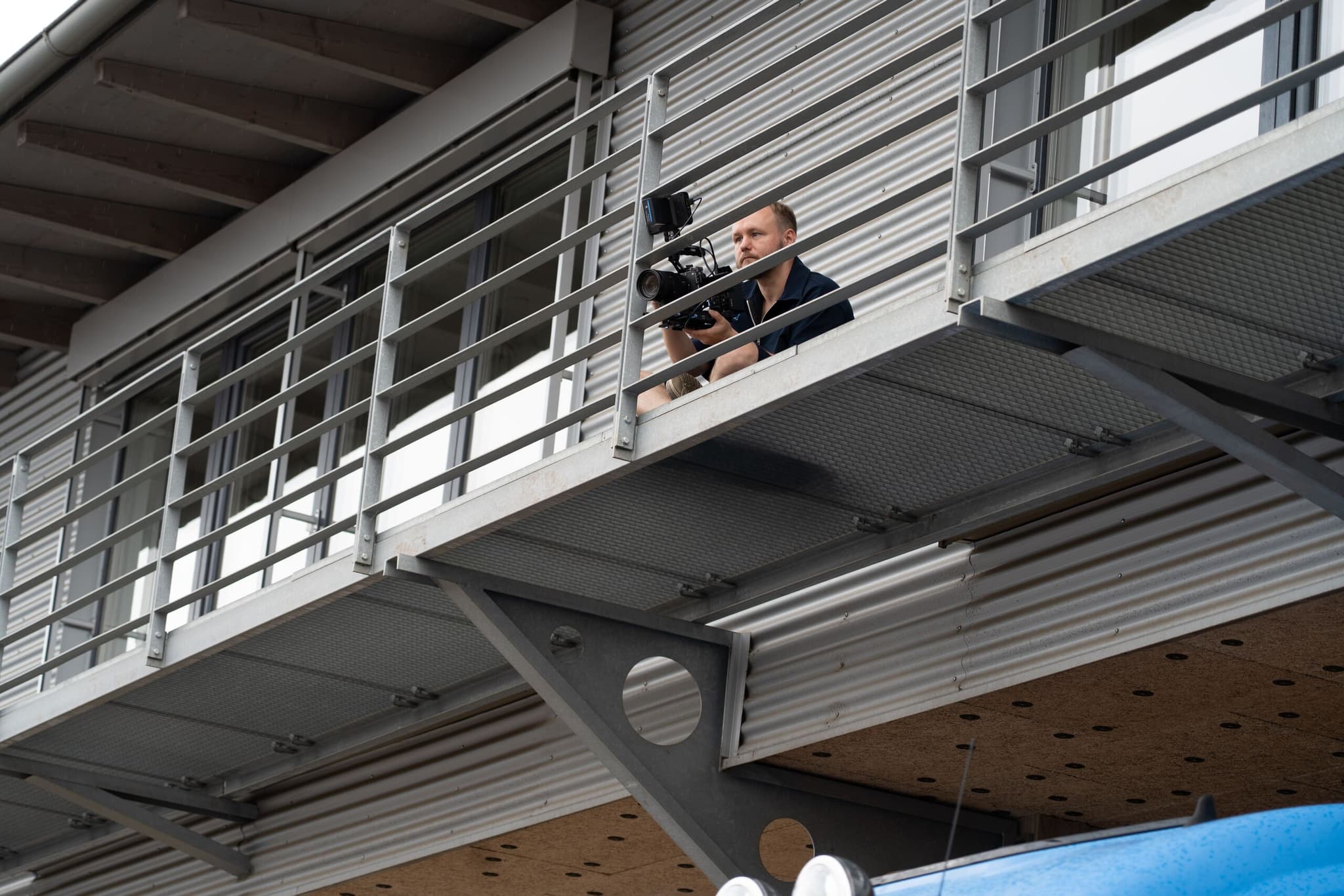 Kameramann mit Videokamera auf einer Stahlgalerie an der Fertigungshalle, von unten aufgenommen