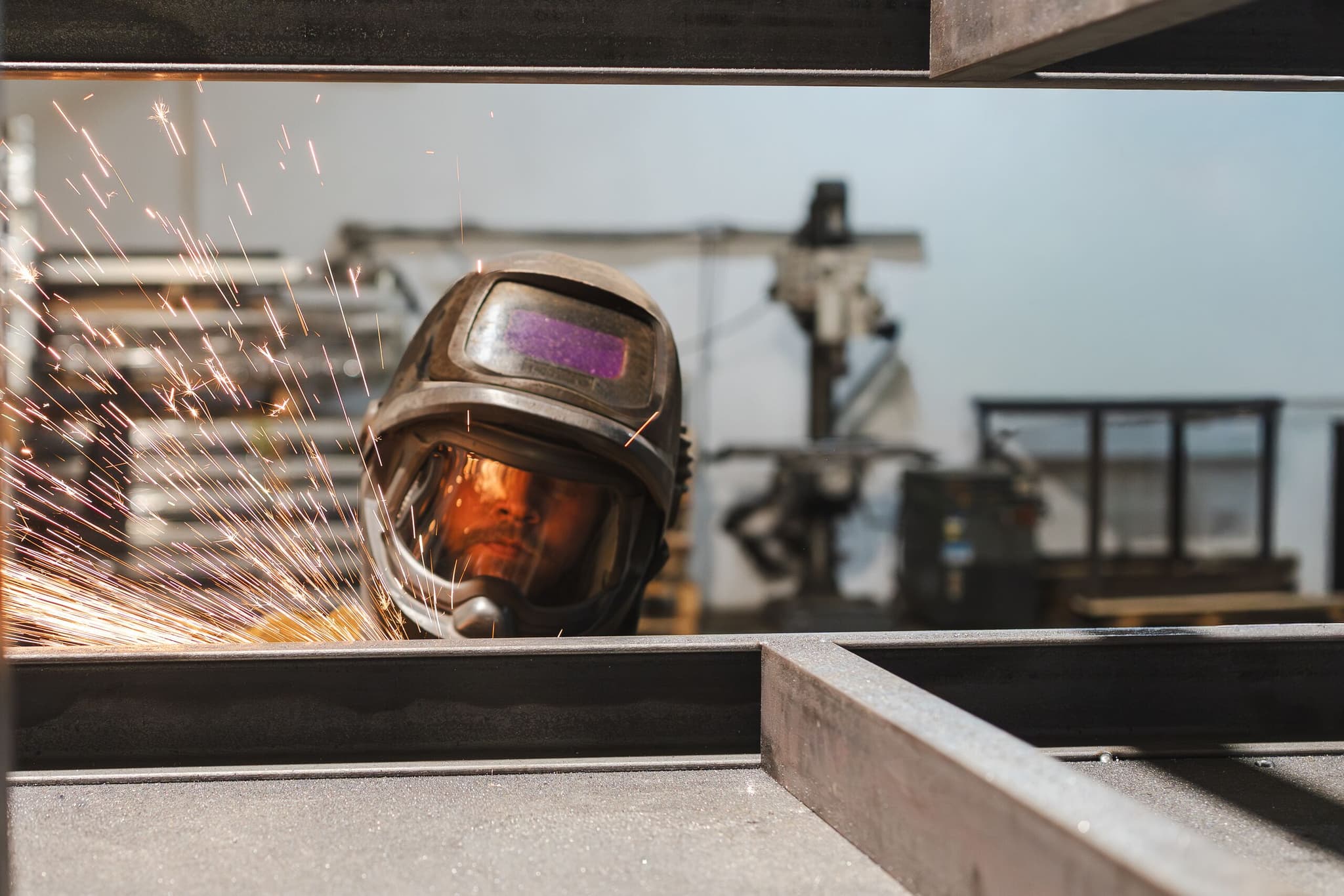 Schweißer mit Schutzhelm hinter Stahlprofilen, Funken sprühen zur Seite